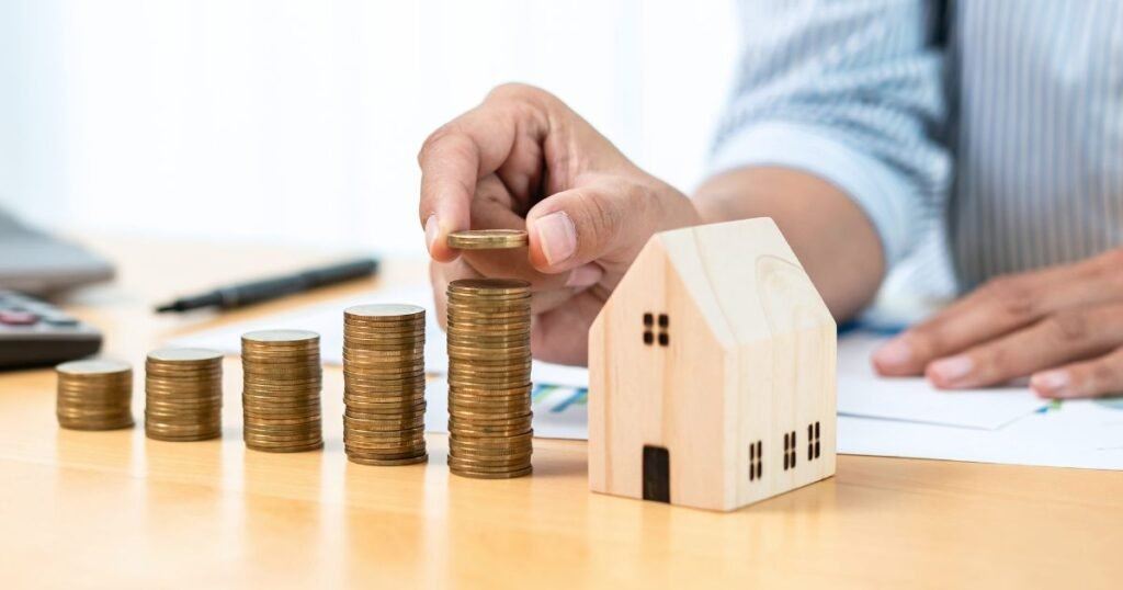 Person stacking of coins next to a small wooden house